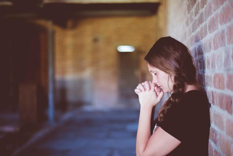 girl praying by a brick wall