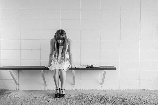 girl sitting head down on bench in front of tile wall